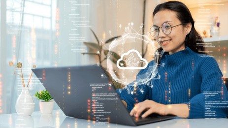 A woman with glasses smiles while using a laptop, with a graphic of a cloud symbol and network connections overlaid to represent cloud computing.