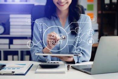 A woman at her desk with a holographic overlay of a network diagram and the words 'ZERO TRUST', symbolising the concept of Zero Trust security in an organisation.